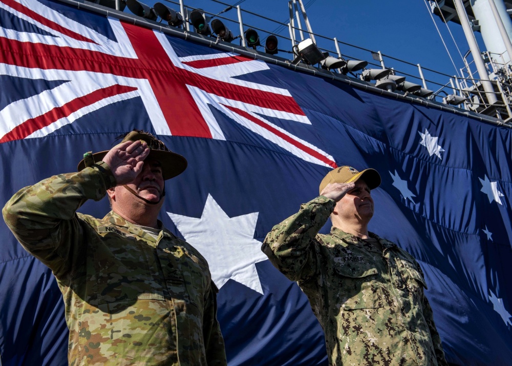 Service members stand at attention in front of the Australian Flag